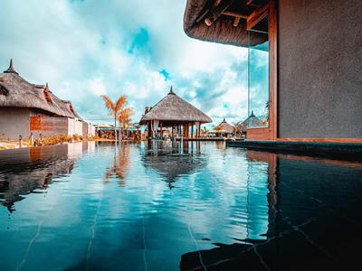 Luxusní bungalovy na vodě a bazén pod zamračenou oblohou v tropické destinaci.