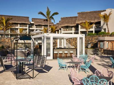 Outdoor-Lounge-Bereich mit Sitzgelegenheiten und Palmen vor Hotelgebäude bei blauem Himmel