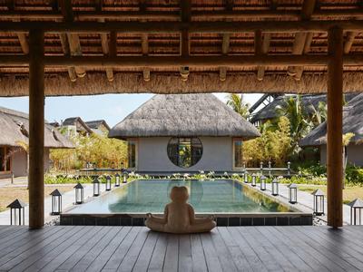Person sitzt auf Holzterrasse mit Blick auf Pool und strohgedeckte Hütten in tropischer Umgebung