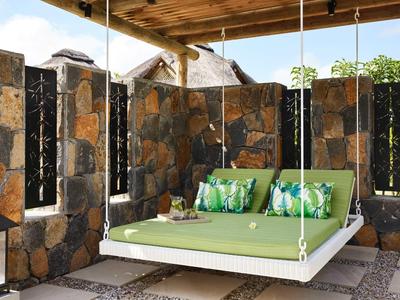 Závěsná postel se zelenou matrací a polštáři v kamenném pavilonu s střechou.