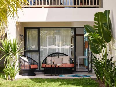 Moderní hotelový pokoj s terasou, dvěma křesly a pohovkou, obklopený zelenými rostlinami.