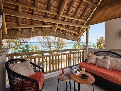 Zastřešená terasa s křesly a pohovkou s výhledem na moře a stromy.