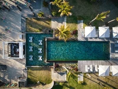 Letecký pohled na obdélníkový bazén s lehátky a palmami v hotelové zahradě.