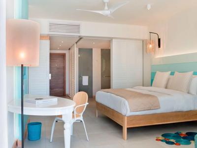 Světle zařízený hotelový pokoj s manželskou postelí, židlí, psacím stolem, moderním osvětlením a klimatizací.