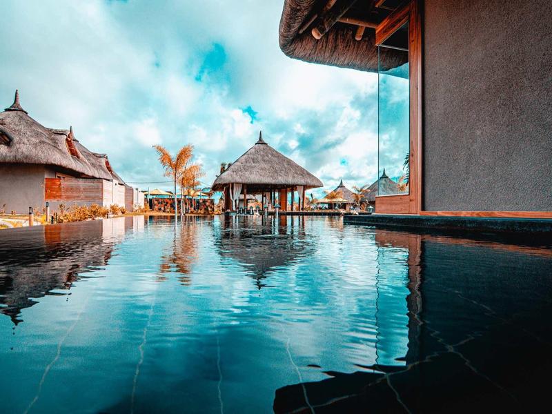 Luxusní bungalovy na vodě a bazén pod zamračenou oblohou v tropické destinaci.