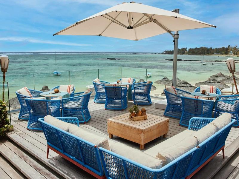 Příjemná venkovní lounge s modrým nábytkem a slunečníkem u moře.