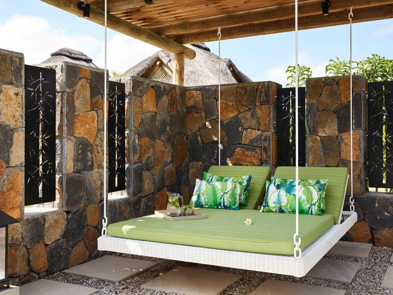Závěsná postel se zelenou matrací a polštáři v kamenném pavilonu s střechou.