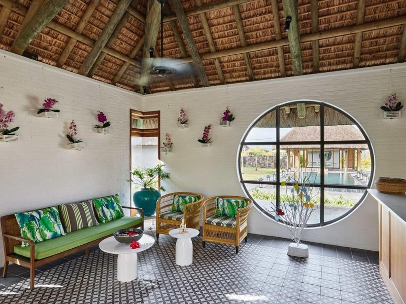 Světý interiér s kulatým oknem, ratanovým nábytkem a tropickou výzdobou.