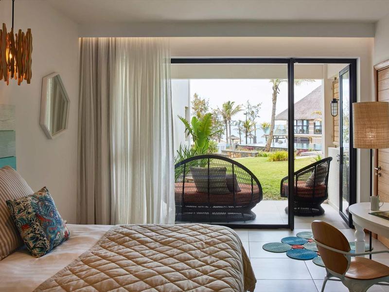 Hotelový pokoj s manželskou postelí, křesly a výhledem na terasu se zahradou.