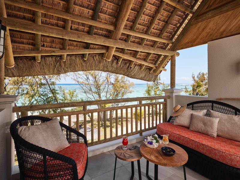 Zastřešená terasa s křesly a pohovkou s výhledem na moře a stromy.