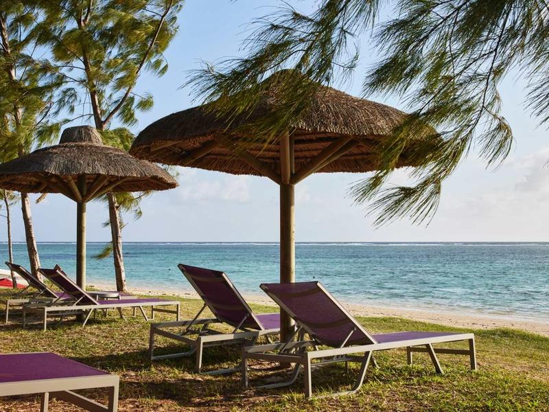 Slunečníky a lehátka na trávníku s výhledem na moře za jasného dne.