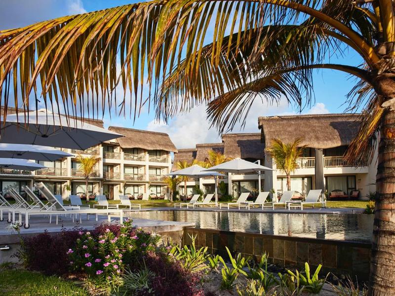 Hotelový komplex s bazénem, palmami a lehátky pod modrou oblohou