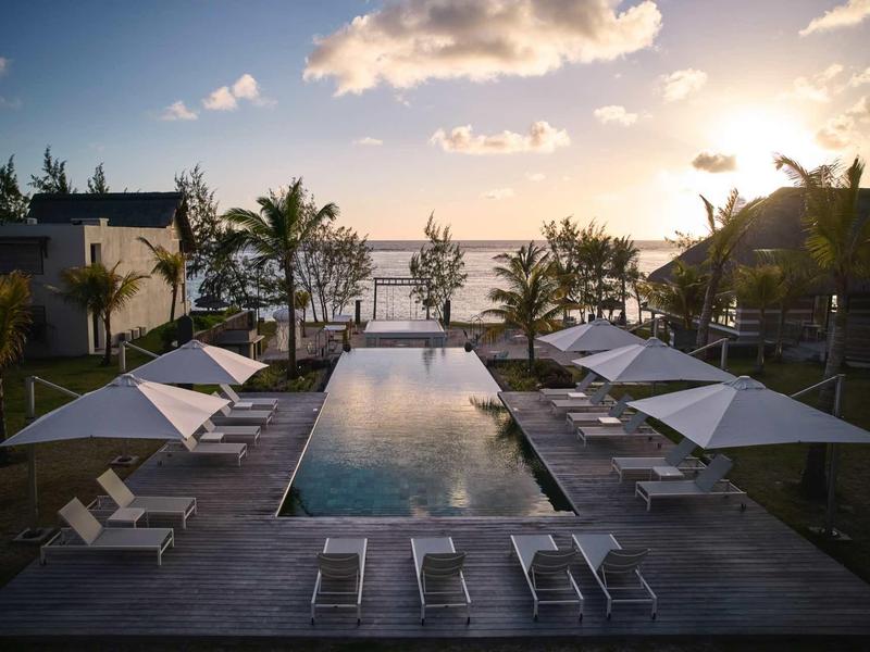 Infinity bazén s lehátky a slunečníky při západu slunce s výhledem na moře.