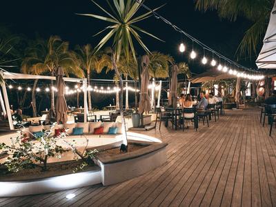 Abendlicher Außenbereich eines Restaurants mit Lichterketten, Holzfußboden und Palmen.