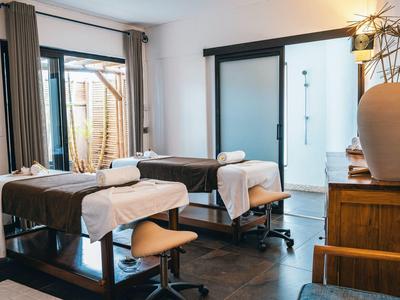 A bright treatment room with two massage beds and chairs in a wellness hotel.