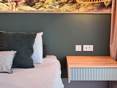 Modern bedroom with gray wall, wooden nightstand, and decorative hanging lamp.