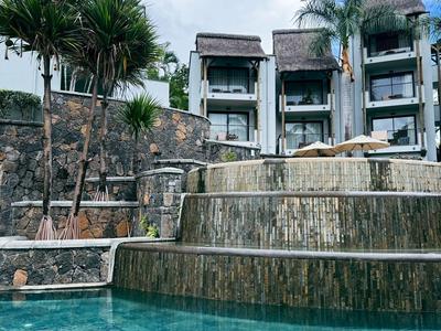 Mehrstöckiger Hotelkomplex mit einem Wasserfall und klarem Pool im Vordergrund.