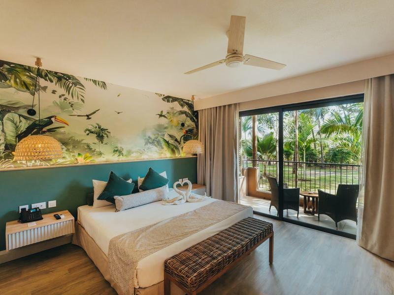 Modern hotel room with double bed, balcony, and tropical view