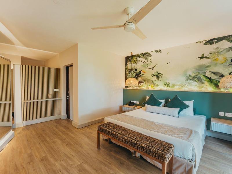 Modern hotel room with double bed, wooden bench, wall mural, and ceiling fan.