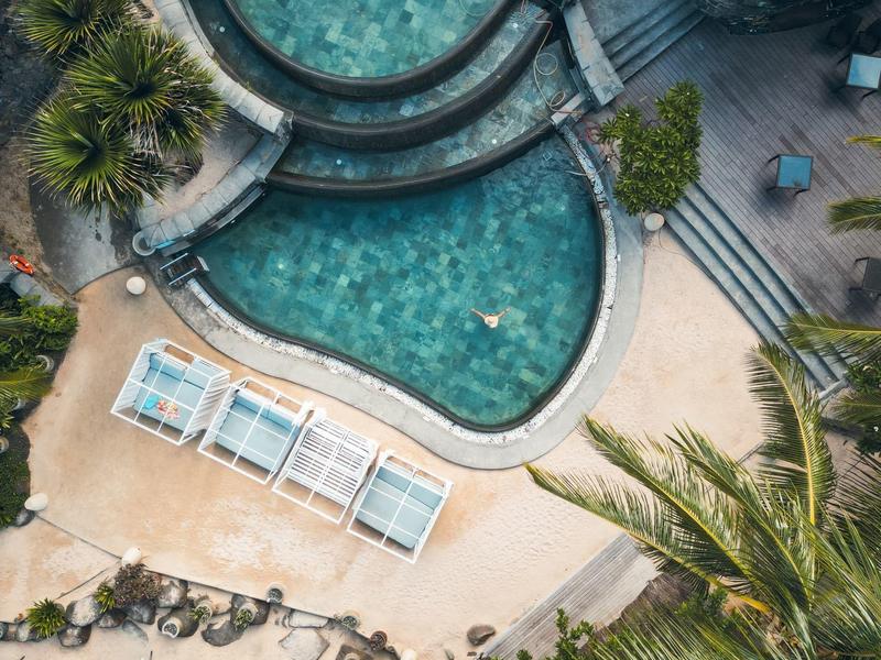 Aerial view of a hotel pool surrounded by lounge chairs and palm trees.
