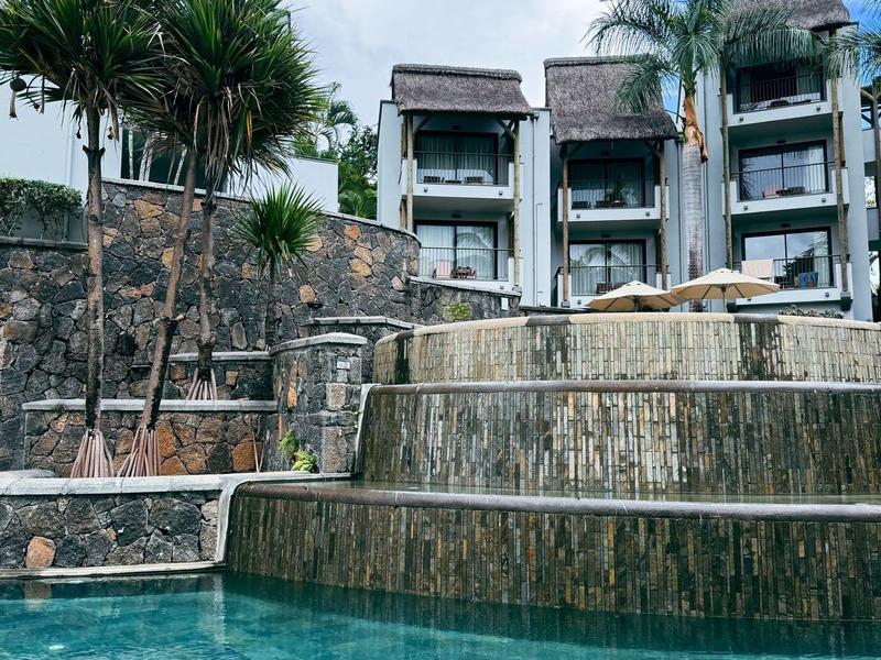 Multi-level pool with waterfall in front of modern hotel rooms and palm trees.