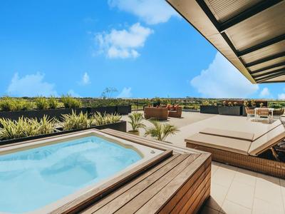 Area esterna moderna con vasca idromassaggio, lettini e piante sotto il cielo azzurro.