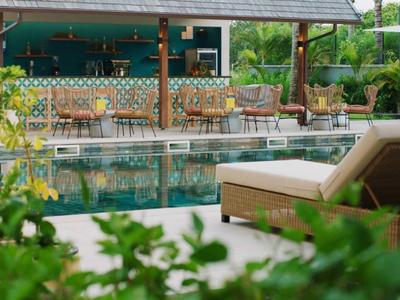 Accogliente zona piscina con sedia a sdraio e bar sullo sfondo, circondata da vegetazione.