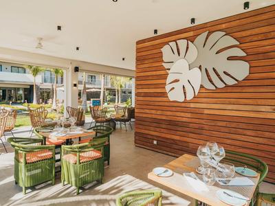 Ristorante luminoso con decorazioni in legno e sedie verdi imbottite vicino a grandi finestre.