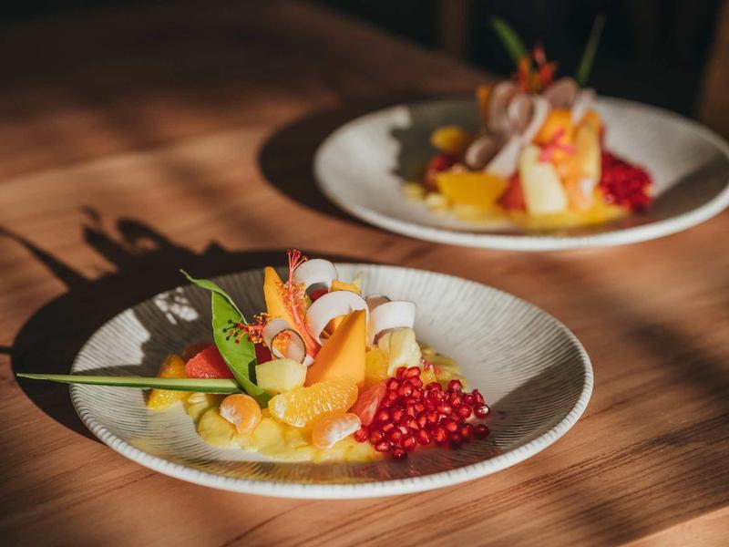 Due piatti artisticamente impiattati con insalata di frutta su un tavolo di legno alla luce del sole.