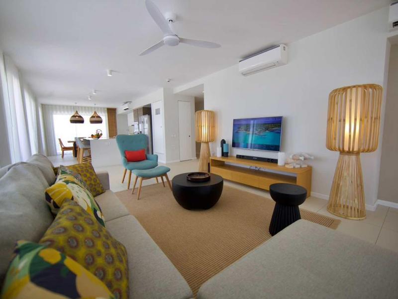 Soggiorno luminoso con mobili moderni, tappeto e ventilatori a soffitto in un appartamento vacanze.