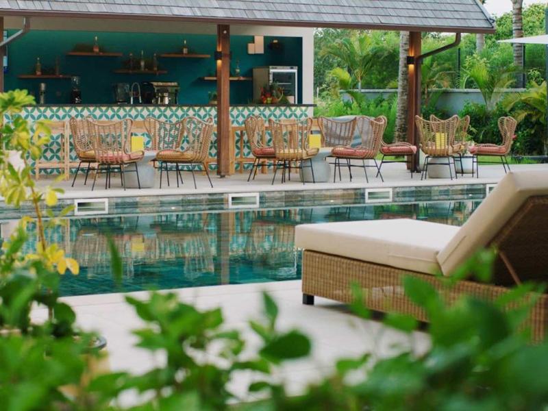 Accogliente zona piscina con sedia a sdraio e bar sullo sfondo, circondata da vegetazione.