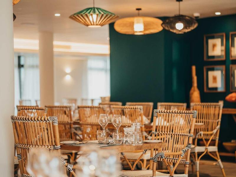 Sala da pranzo moderna con sedie in vimini e tavoli apparecchiati.