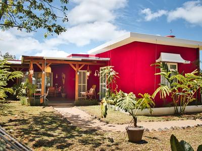 Rotes Ferienhaus mit überdachter Terrasse und Garten bei sonnigem Himmel.