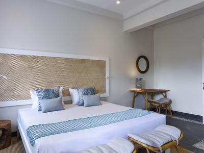 Schlafzimmer mit großem Bett, weißen Wänden, Holzstuhl, Rundspiegel und hellblauem Bettläufer.