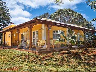 Einfamilienhaus mit gelber Fassade, braunen Holzbalken und Terrasse unter blauem Himmel.