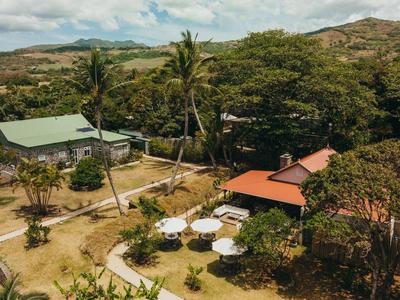 Landschaft mit mehreren Gebäuden, Palmen, Bäumen und Wegen unter blauem Himmel mit Wolken.