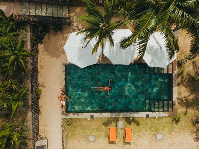 Vogelperspektive eines Pools mit Person, Palmen und Liegestühlen in einem tropischen Resort.
