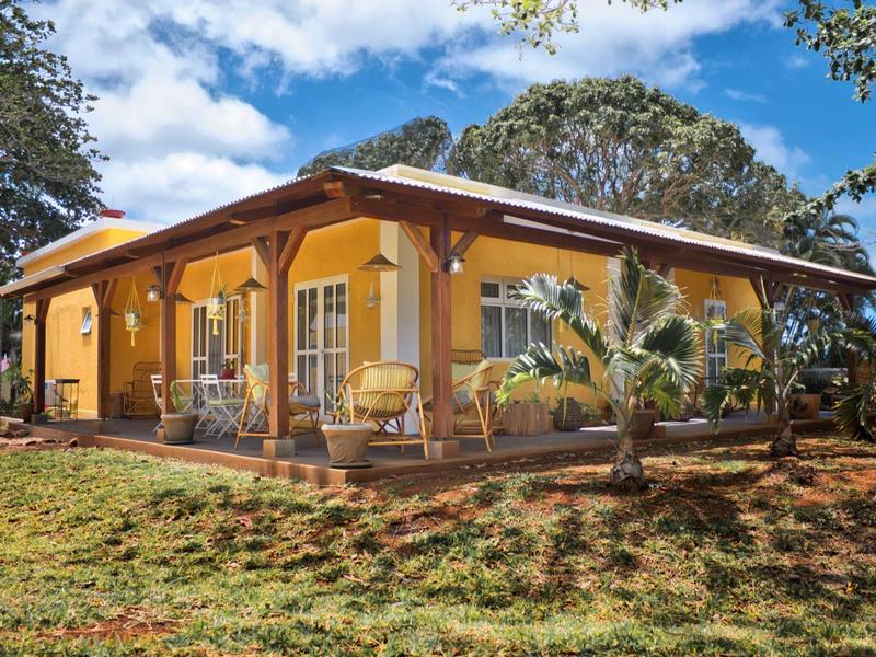 Einfamilienhaus mit gelber Fassade, braunen Holzbalken und Terrasse unter blauem Himmel.