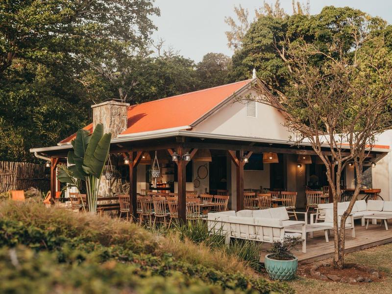 Gemütliches Holzhaus mit rotem Dach, umgeben von Bäumen und Garten in warmem Licht.