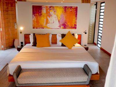 Světlý hotelový pokoj s velkou postelí, barevným obrazem a lavicí u nohou.