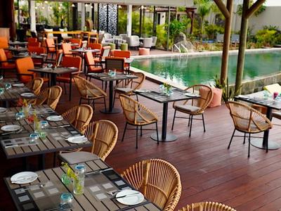 Moderní venkovní prostor hotelu s jídelními stoly a bazénem se slunečními lehátky.