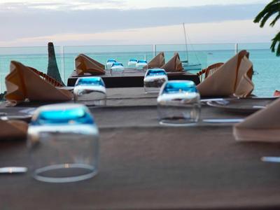 Pohled na prostřené stoly v plážové restauraci s mořem a mraky v pozadí.