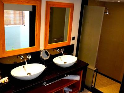 Moderní koupelna se dvěma bílými umyvadly na černé desce a dvěma zrcadly s oranžovými rámy.