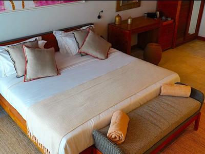 Příjemný hotelový pokoj s velkou manželskou postelí, teplým dřevěným nábytkem a měkkým osvětlením.