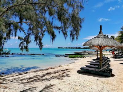 Strand mit Liegestühlen und Sonnenschirmen aus Stroh an klarem, blauem Wasser unter blauem Himmel.