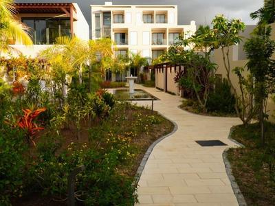 Dlázdená cesta vede zahradou hotelu s rostlinami a stromy pod zataženou oblohou.