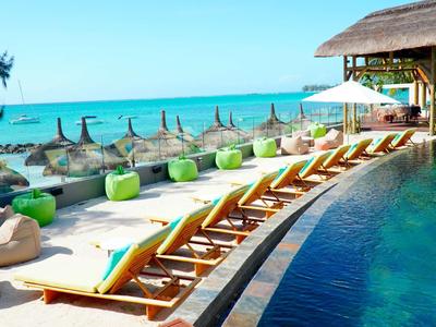 Luxuriöser Poolbereich mit Liegestühlen, Strandkörben und Meerblick bei klarem Himmel.