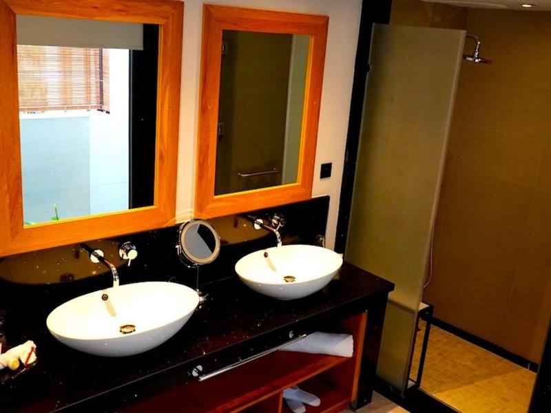 Moderní koupelna se dvěma bílými umyvadly na černé desce a dvěma zrcadly s oranžovými rámy.