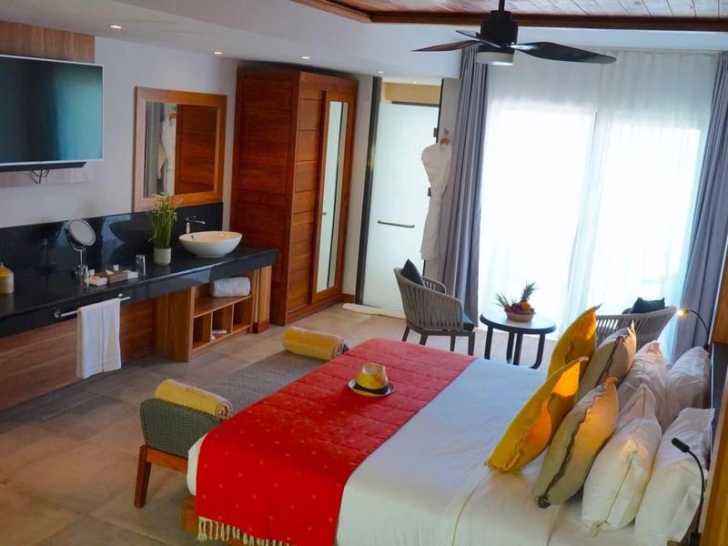 Moderní hotelový pokoj s manželskou postelí, TV, posezením a balkonem se záclonami.