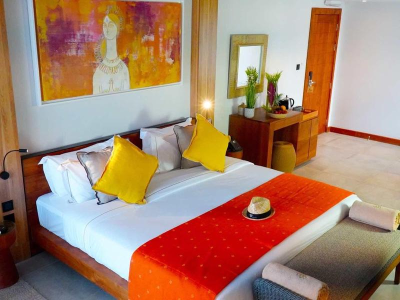 Moderní hotelový pokoj s manželskou postelí, barevnými polštáři a obrazem nad postelí.